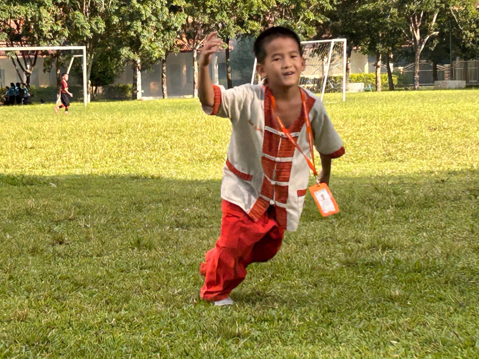 A boy in traditional red and cream Karen dress running across the school field